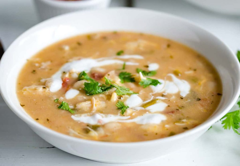 white bowl filled with white chicken chili, garnished with swirls of sour cream and cilantro
