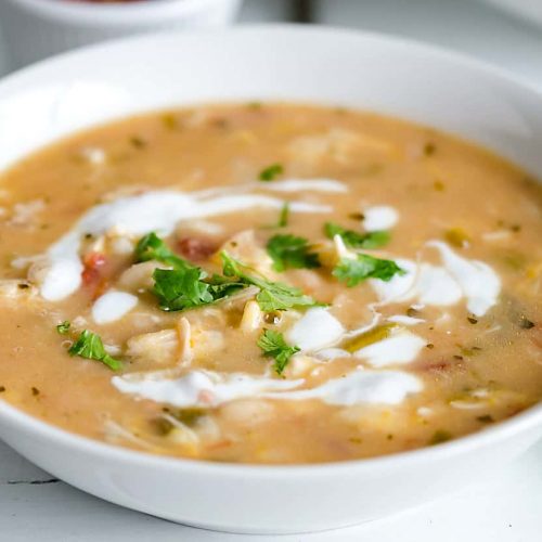white bowl filled with white chicken chili, garnished with swirls of sour cream and cilantro