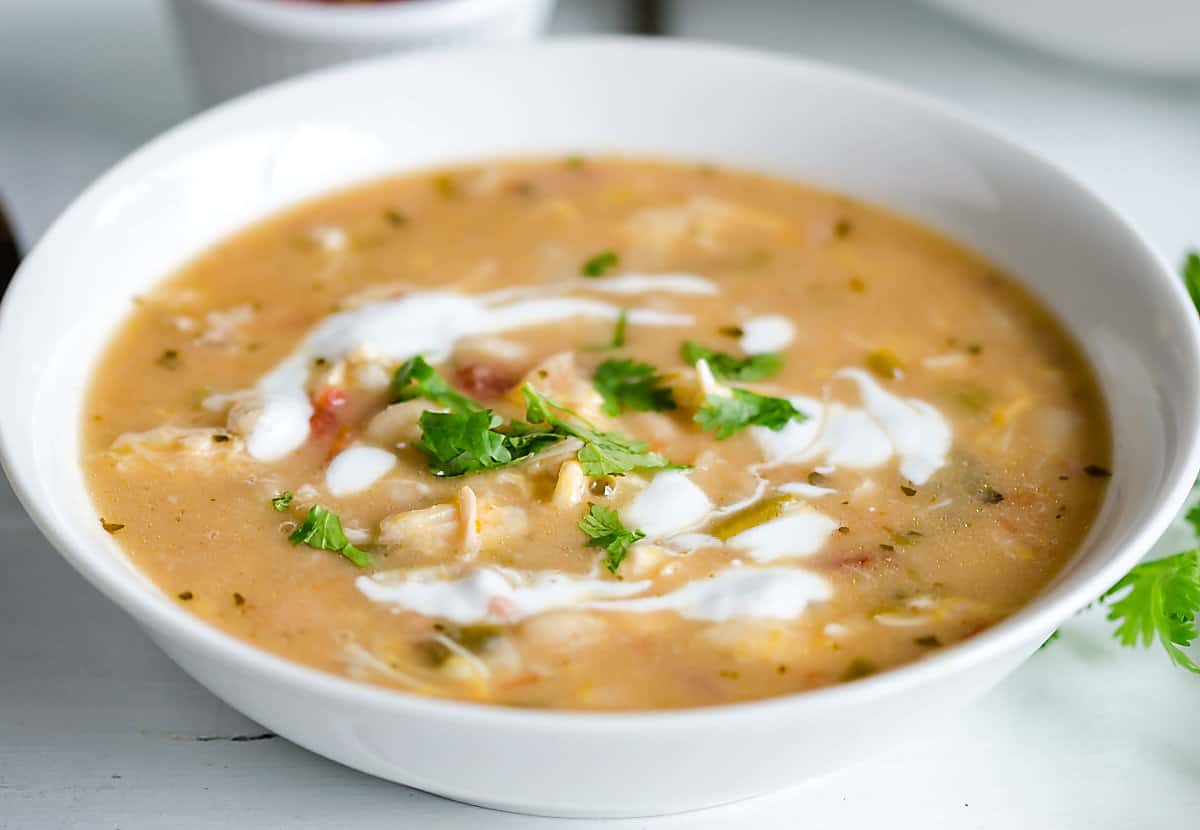 white bowl filled with white chicken chili, garnished with swirls of sour cream and cilantro