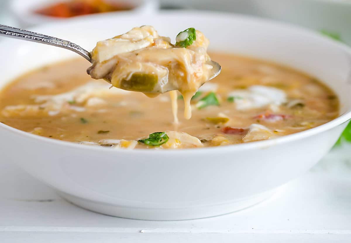 spoonful of white chicken chili hovering over a bowl of chili, cheese dripping off the spoon