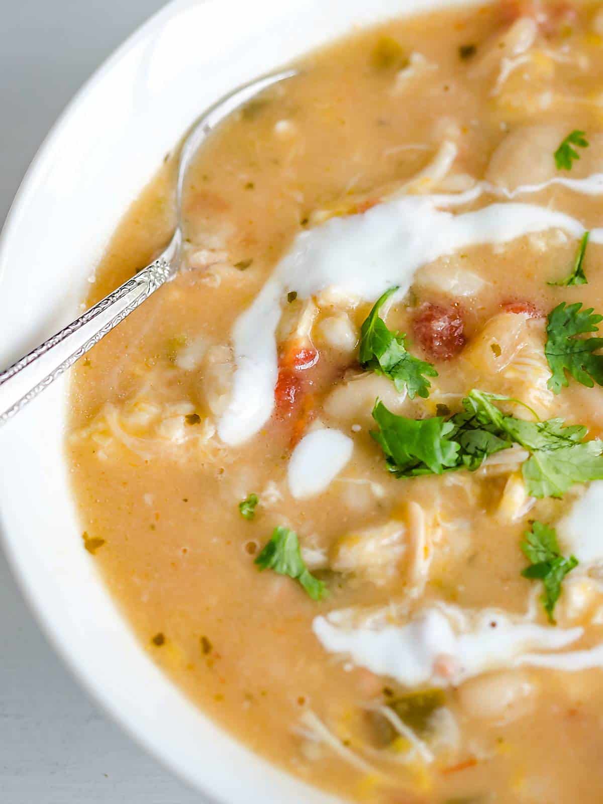 bowl of white chicken chili garnished with cilantro, spoon dipping in.