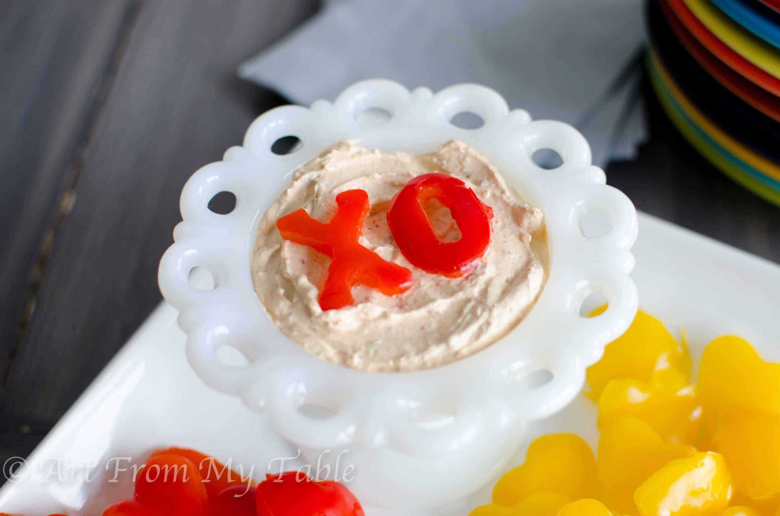 'X' and 'O' cut out of a red bell pepper and placed on top of a healthy vegetable dip for Valentines Day.