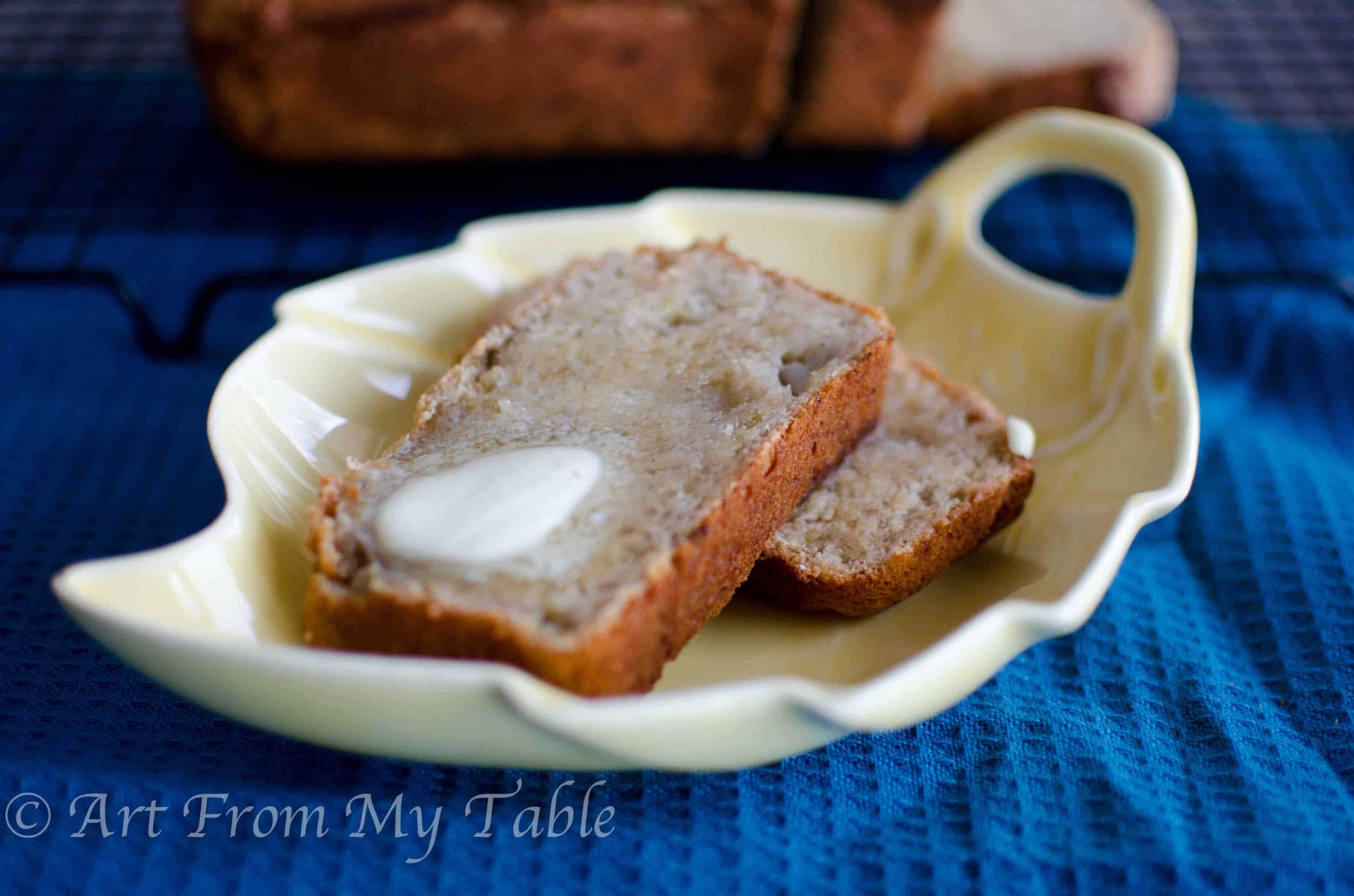 Two slices of homemade banana bread served on a leaf shaped plate with a pat of butter on top.