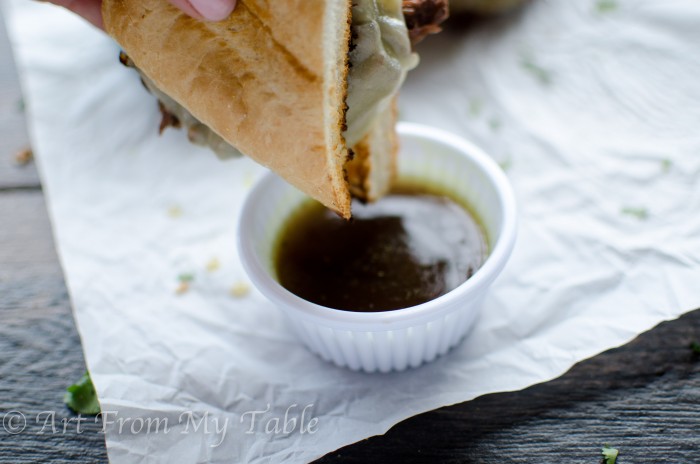 Slow cooker french dip sandwich being dipped in au jus.