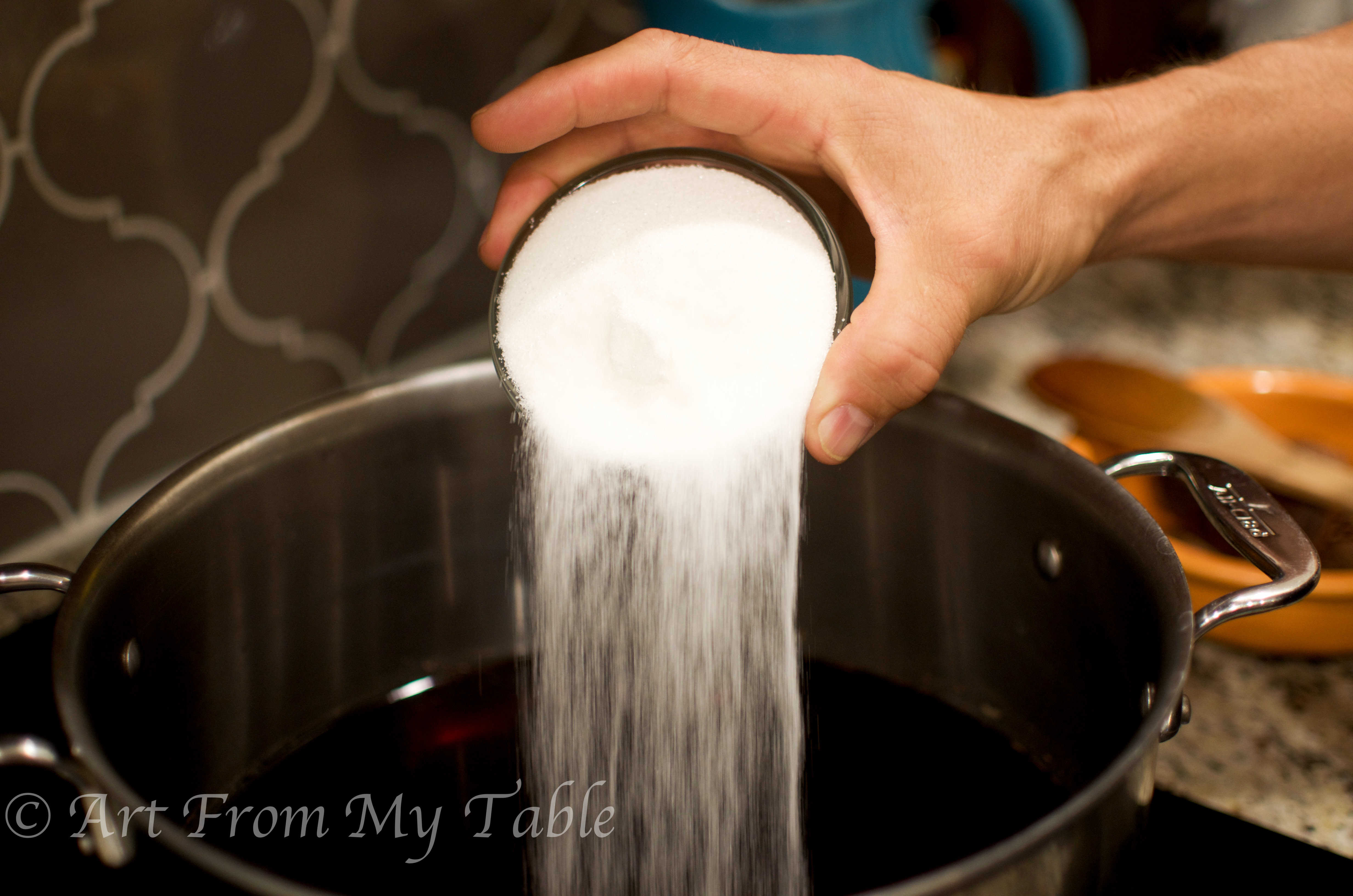 Sugar being poured into the large pot of tea. 