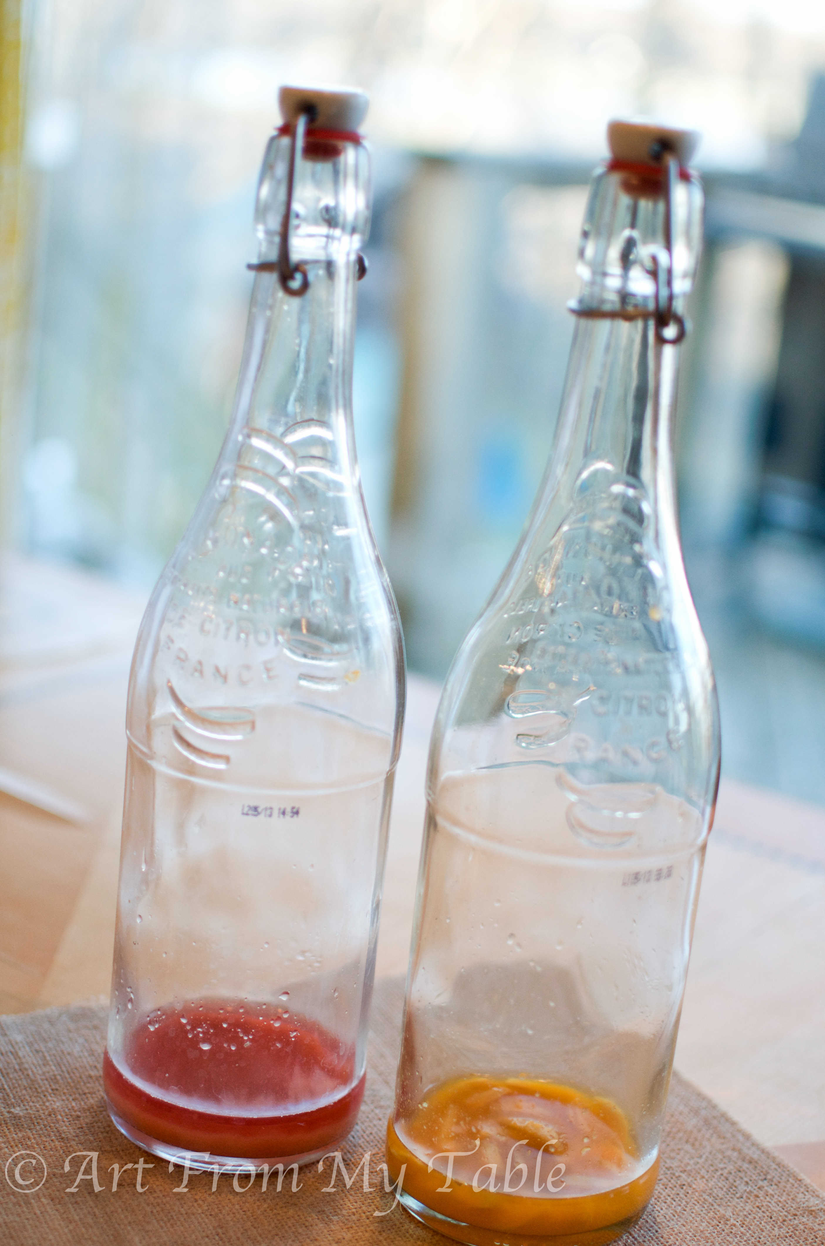 Two glass bottles, one with cherries, and one with orange and ginger flavorings. 