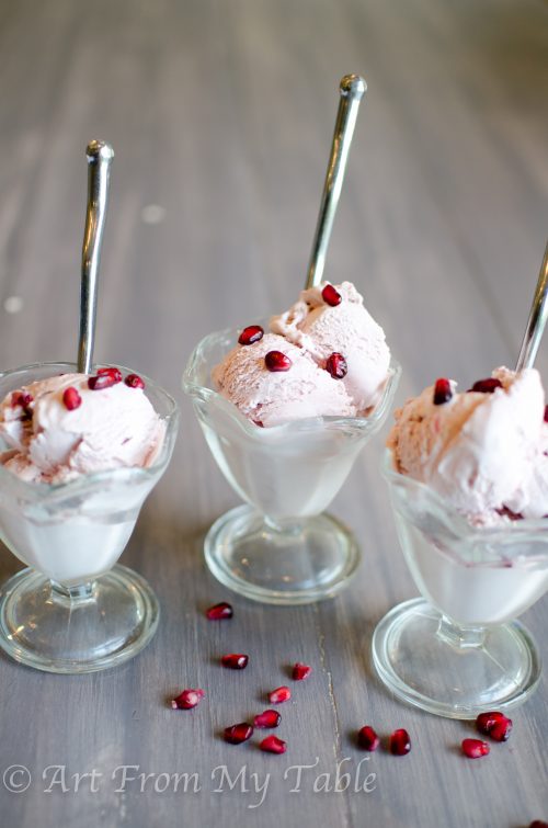 Three dishes of pomegranate ice cream with spoons and pomegranate arils.