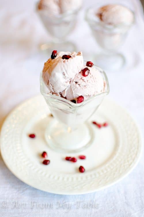 Pomegranate ice cream in a dessert dish with pomegranate arils (seeds) on it.