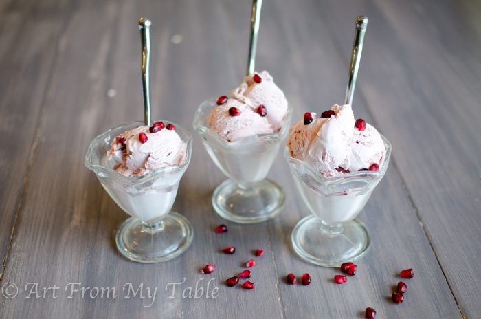 Three dishes pomegranate ice cream with spoons, garnished with pomegranate arils. 