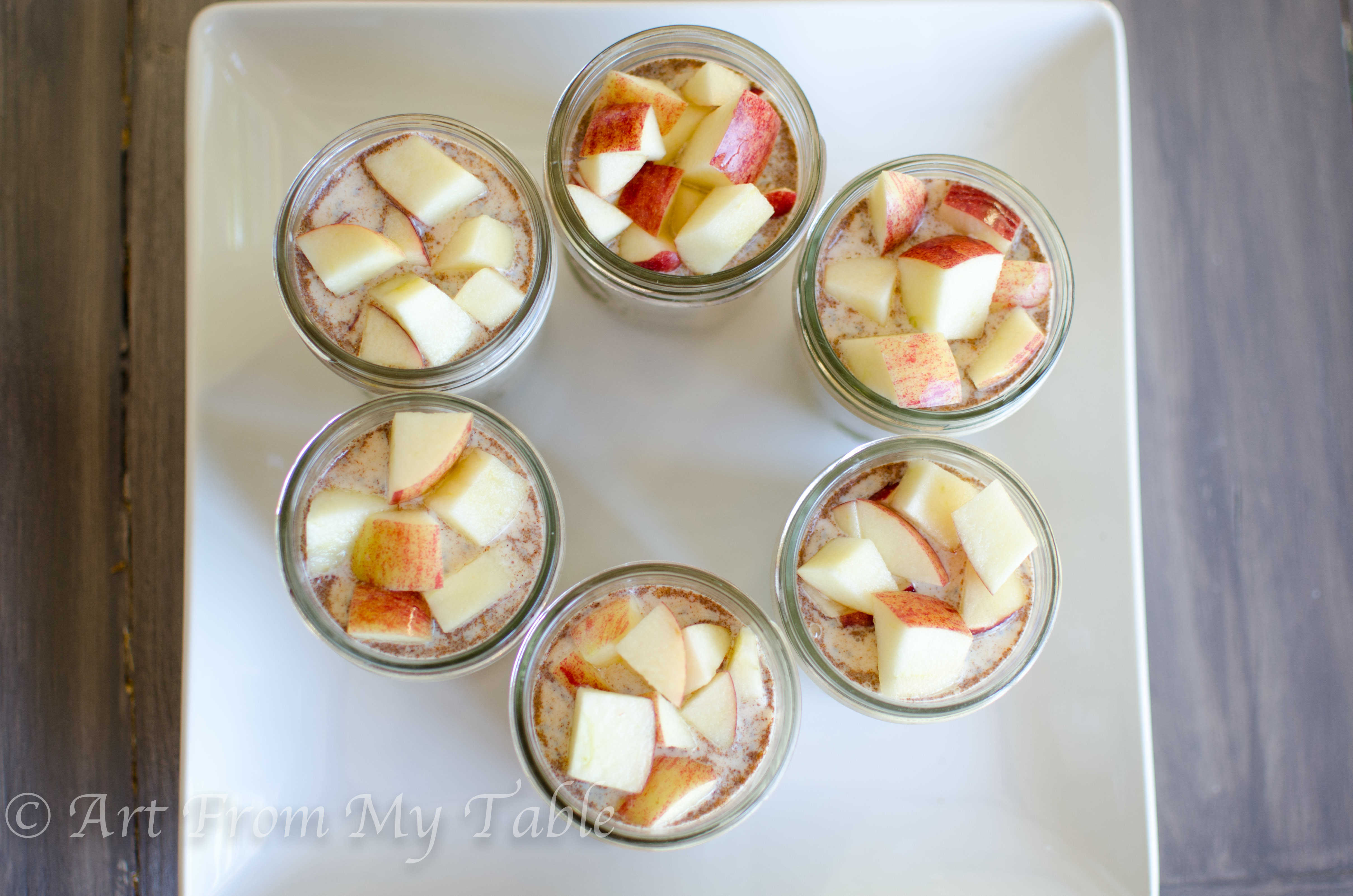 Overnight oats with apples and peanut butter in pint sized mason jars on a platter.
