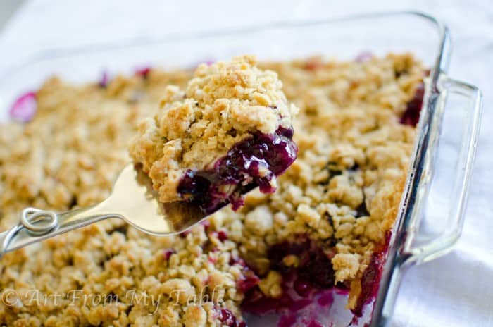baked blueberry peach crisp being scooped from pan