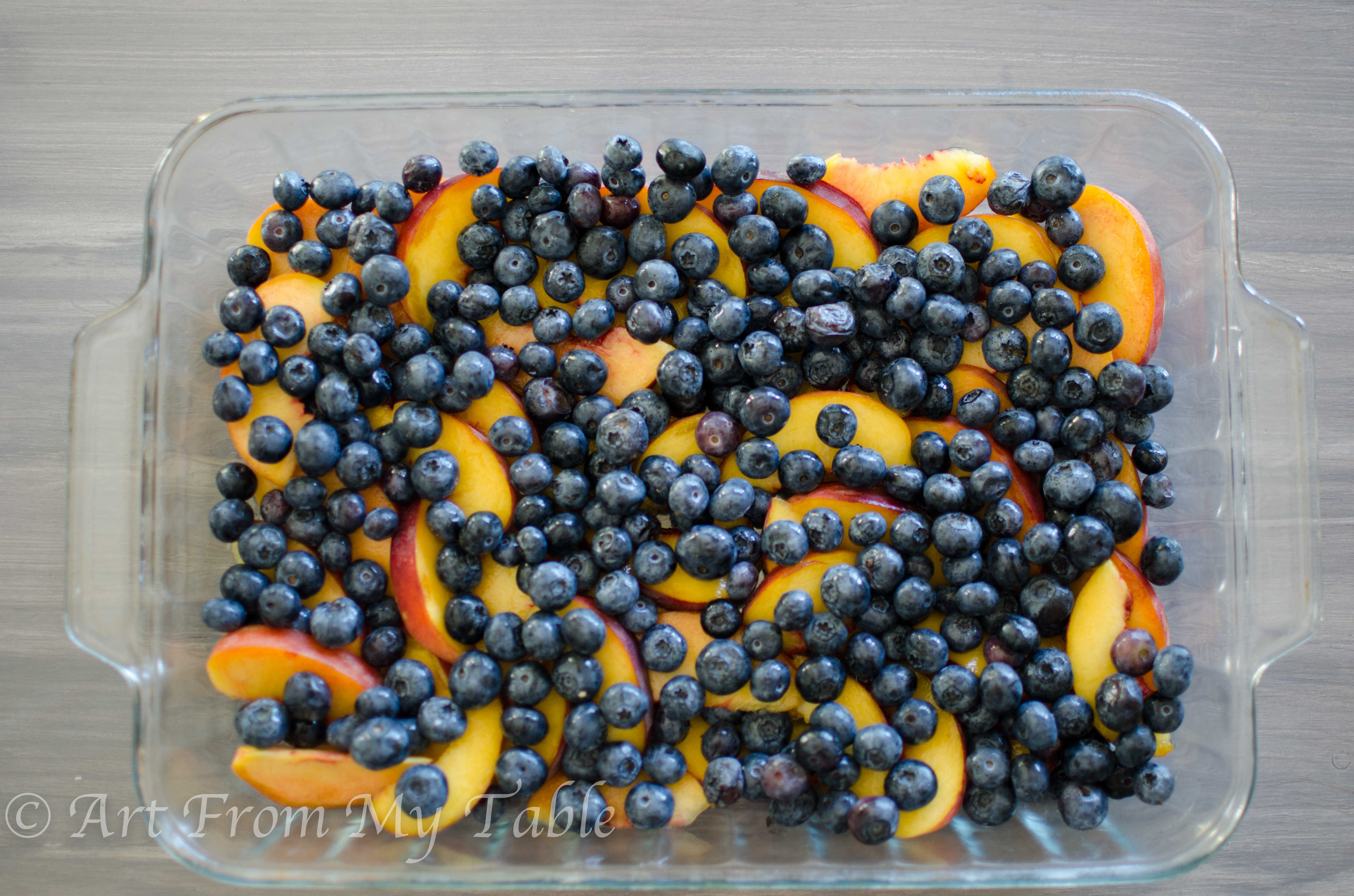 Fresh peaches and fresh blueberries scattered in a 9x13 glass dish.