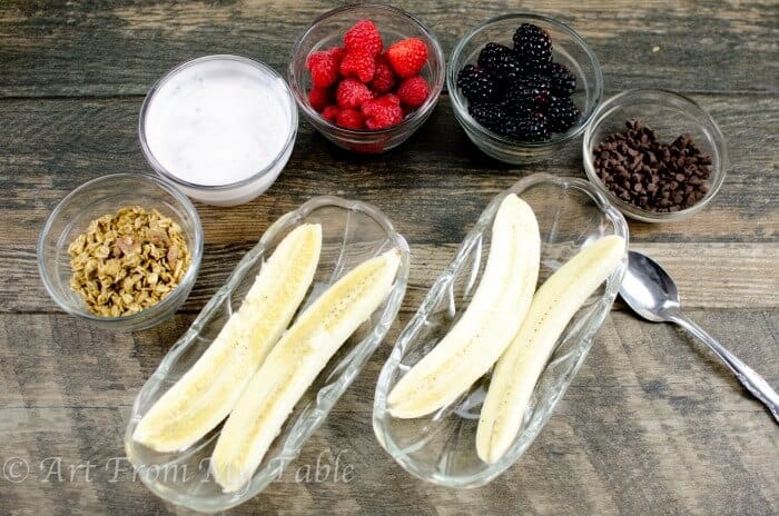 Ingredients for breakfast banana split, bananas, yogurt, berries, granola and chocolate chips. 