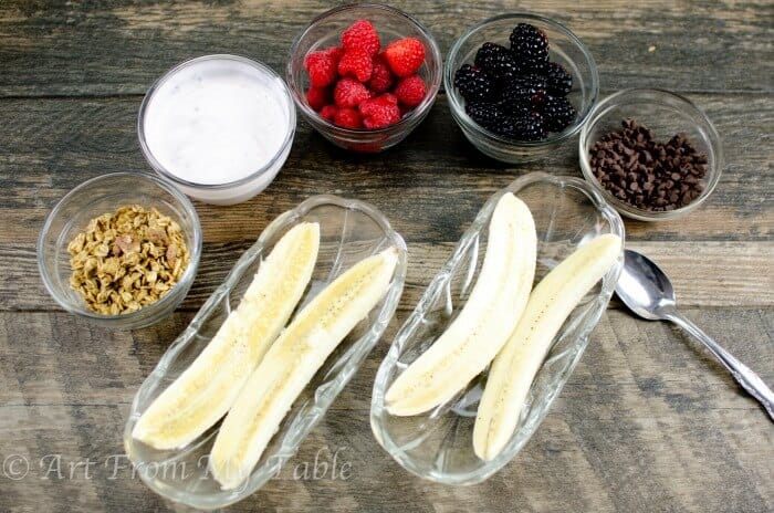 Ingredients for breakfast banana split, bananas, yogurt, berries, granola and chocolate chips.