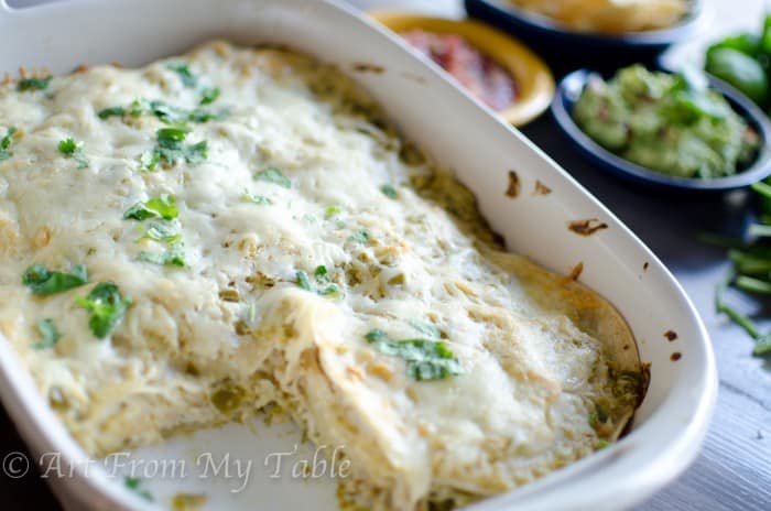 Carnitas casserole verde baked with one piece removed, guacamole and salsa and chips in the background.