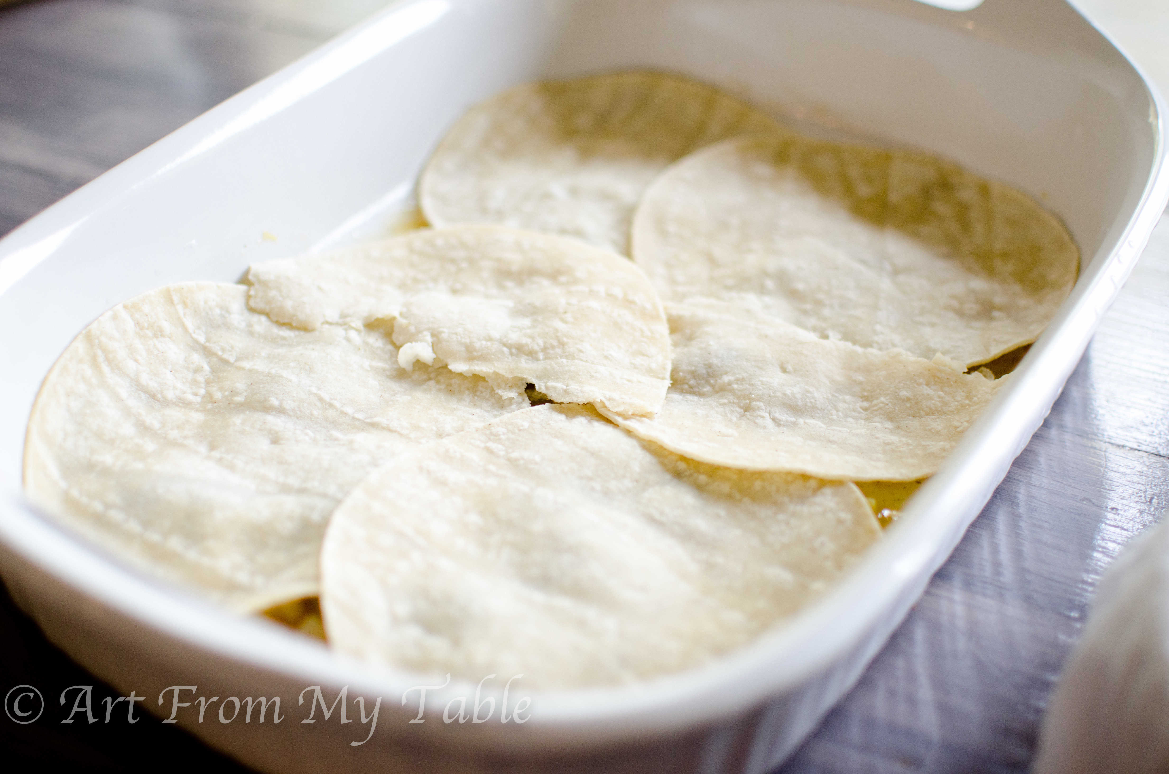 White casserole dish with a layer of soft tortillas over the sauce. 