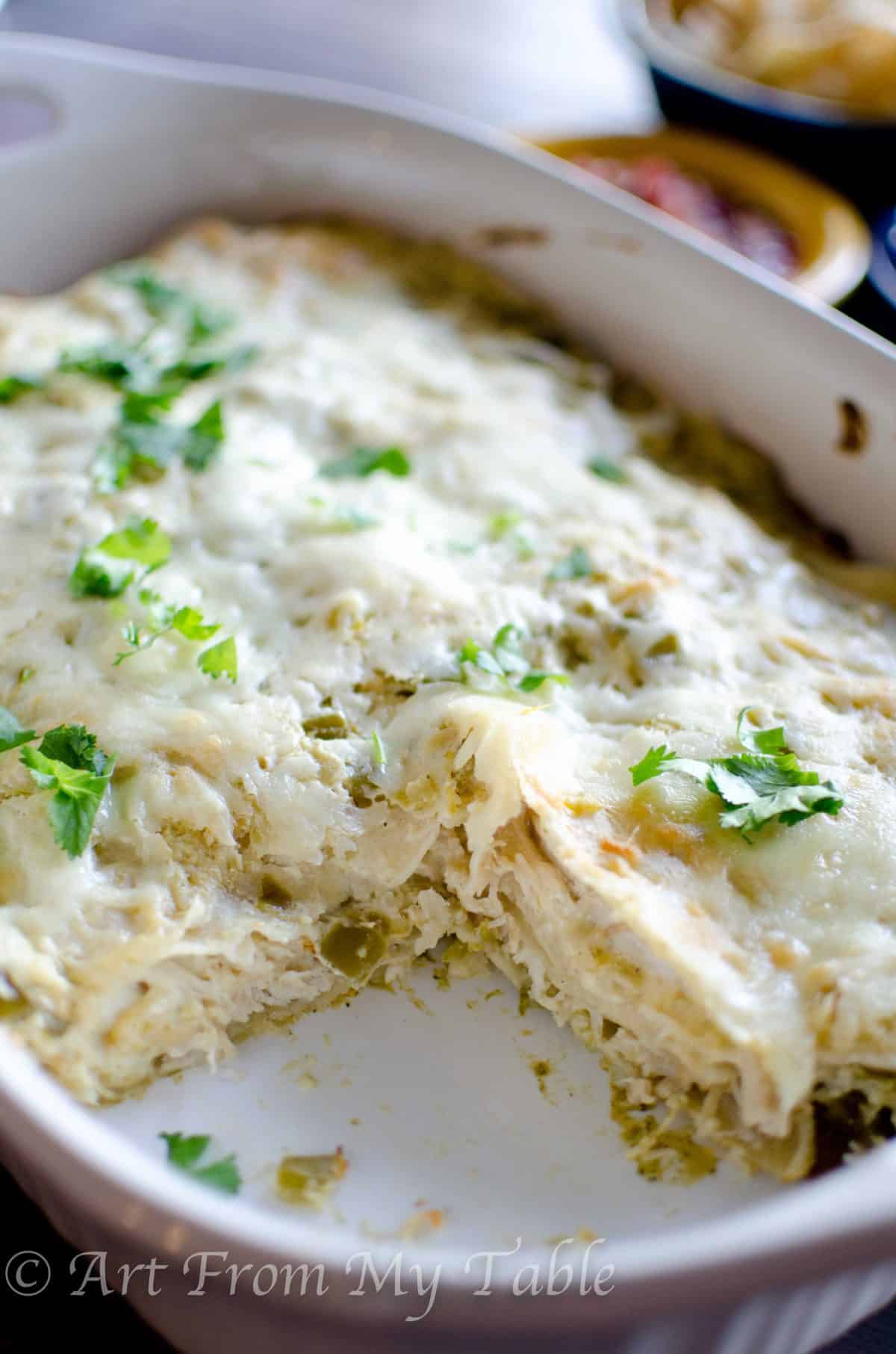 Baked carnitas casserole verde in a white dish with one piece removed.