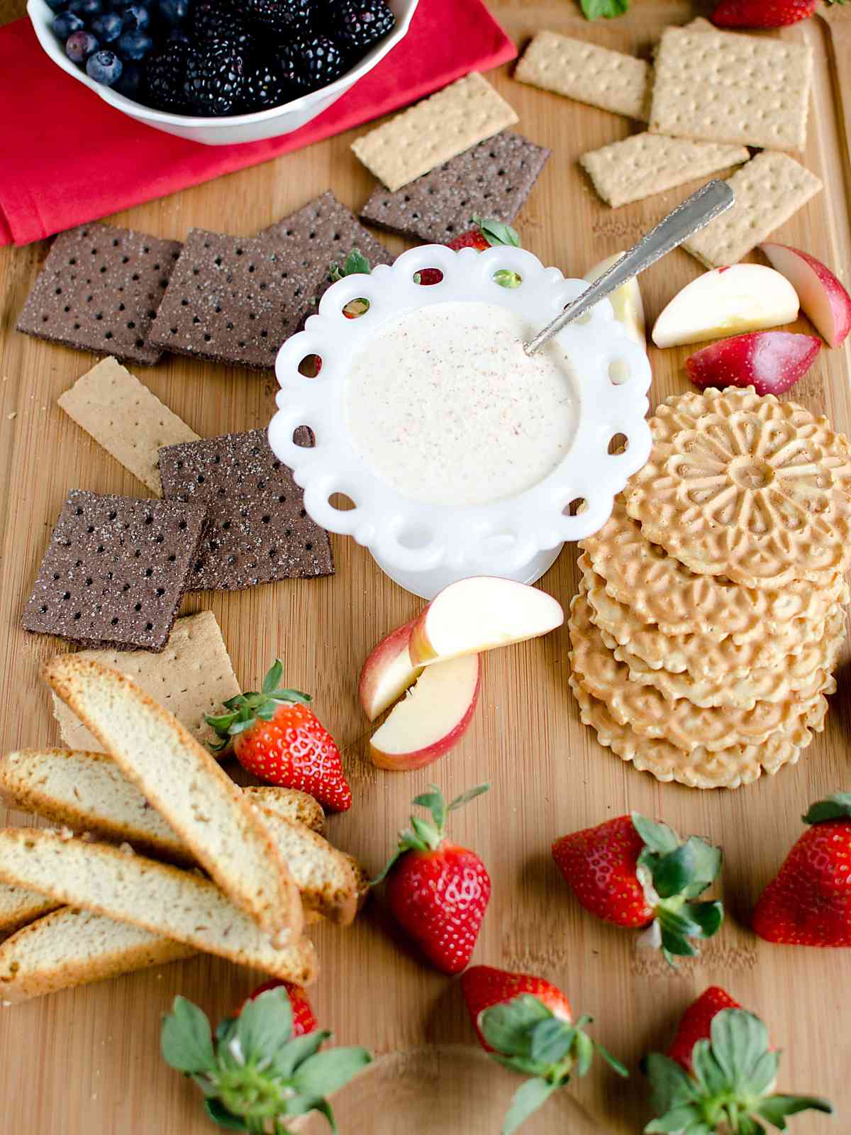 Platter of biscotti, chocolate and plain graham crackers, apples and fruit with a bowl of eggnog dip.