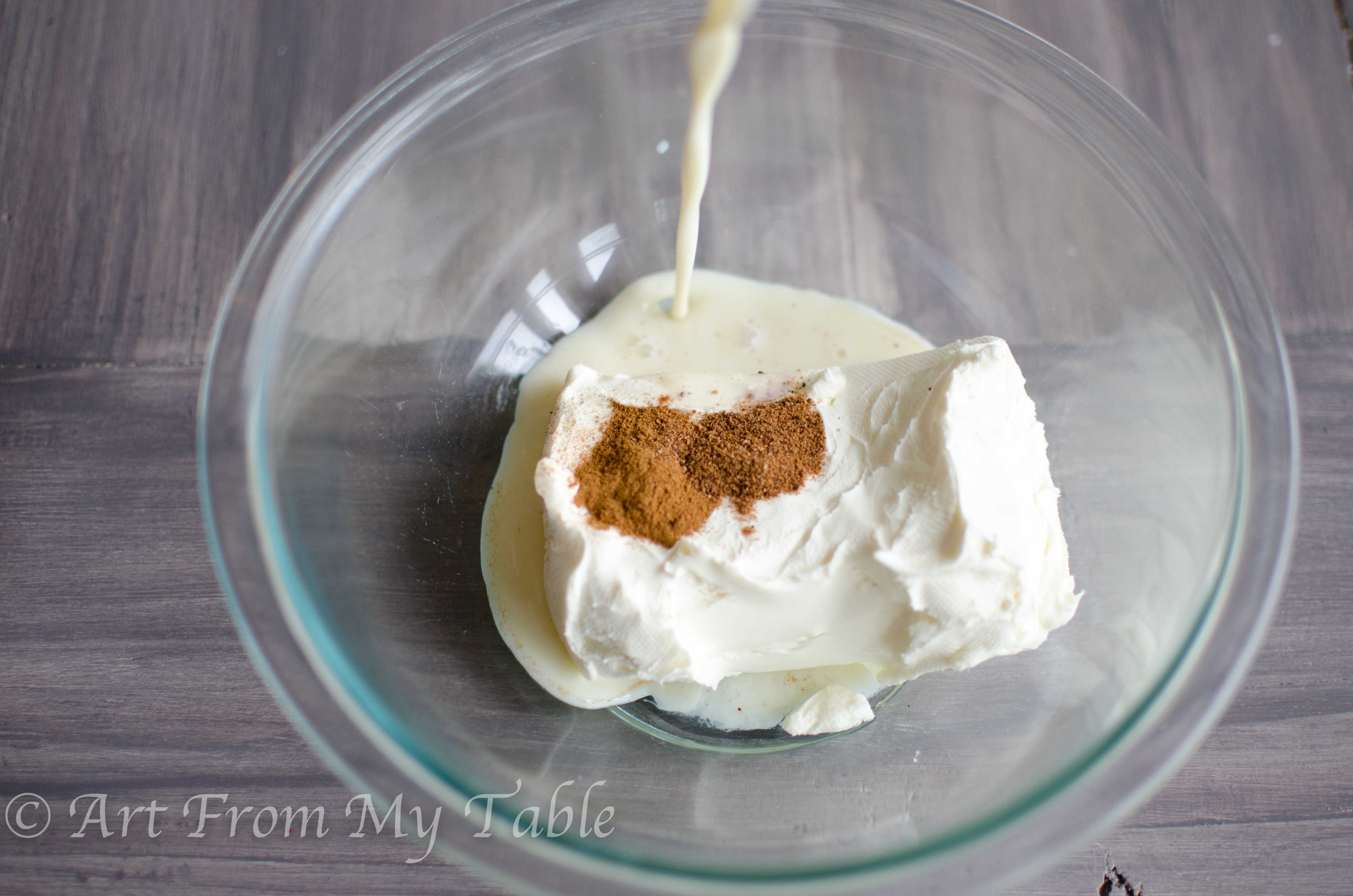 Cream cheese, eggnog, nutmeg, and cinnamon in a bowl before being blended.