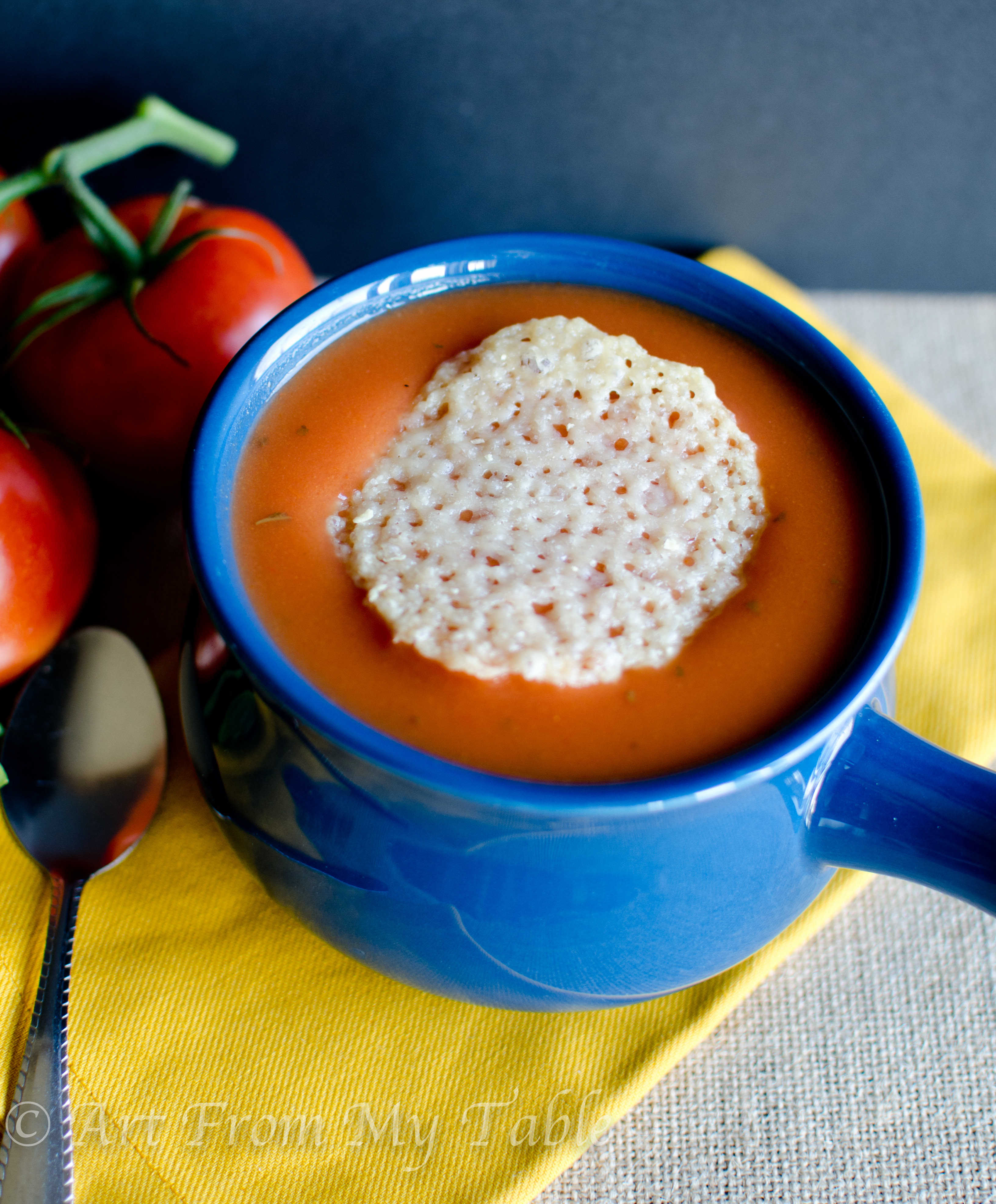 Bowl of tomato soup topped with a Parmesan cheese crisp