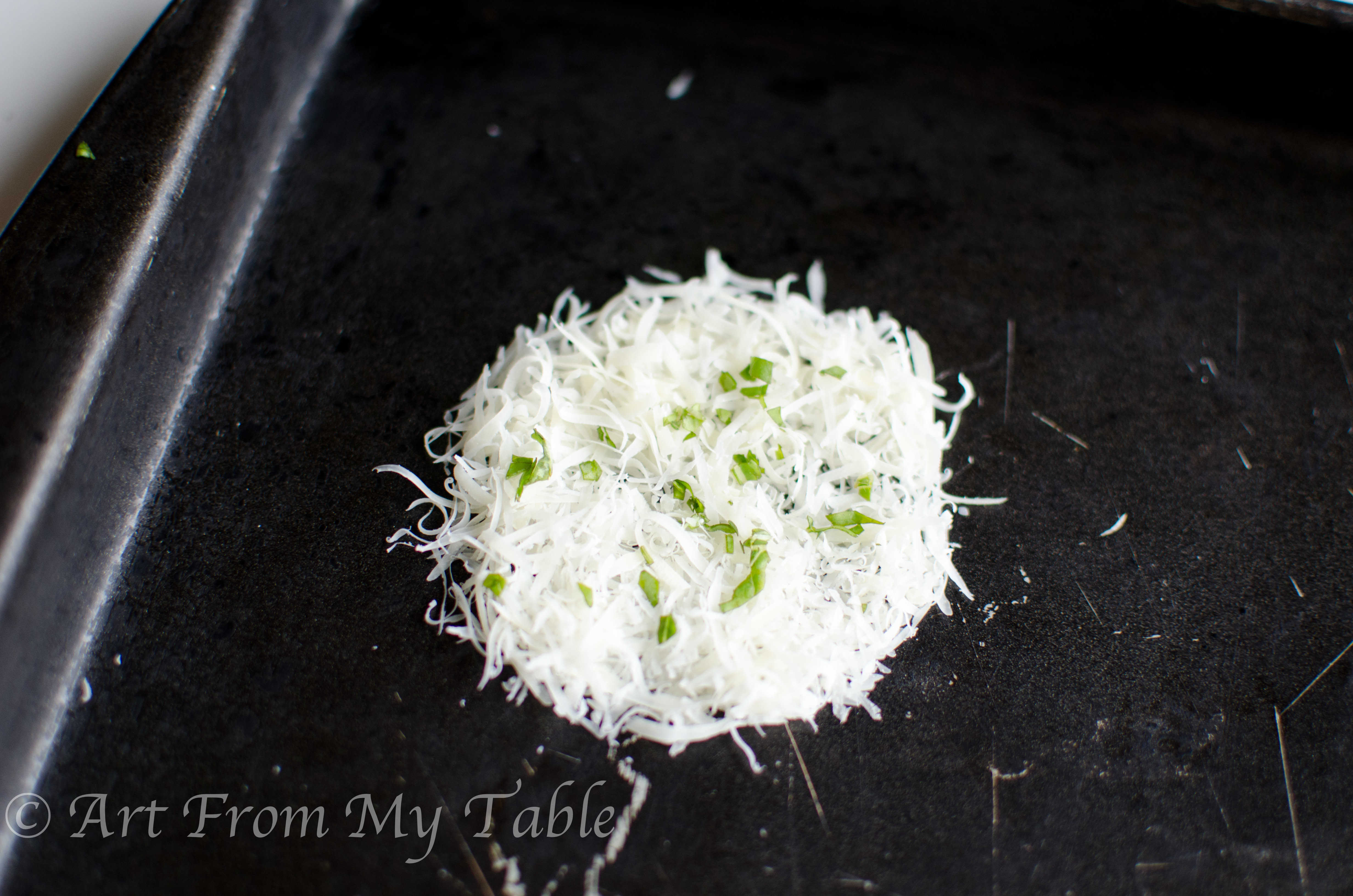 Shredded parmesan cheese formed into a circle on a baking sheet, chopped fresh basil on top. 