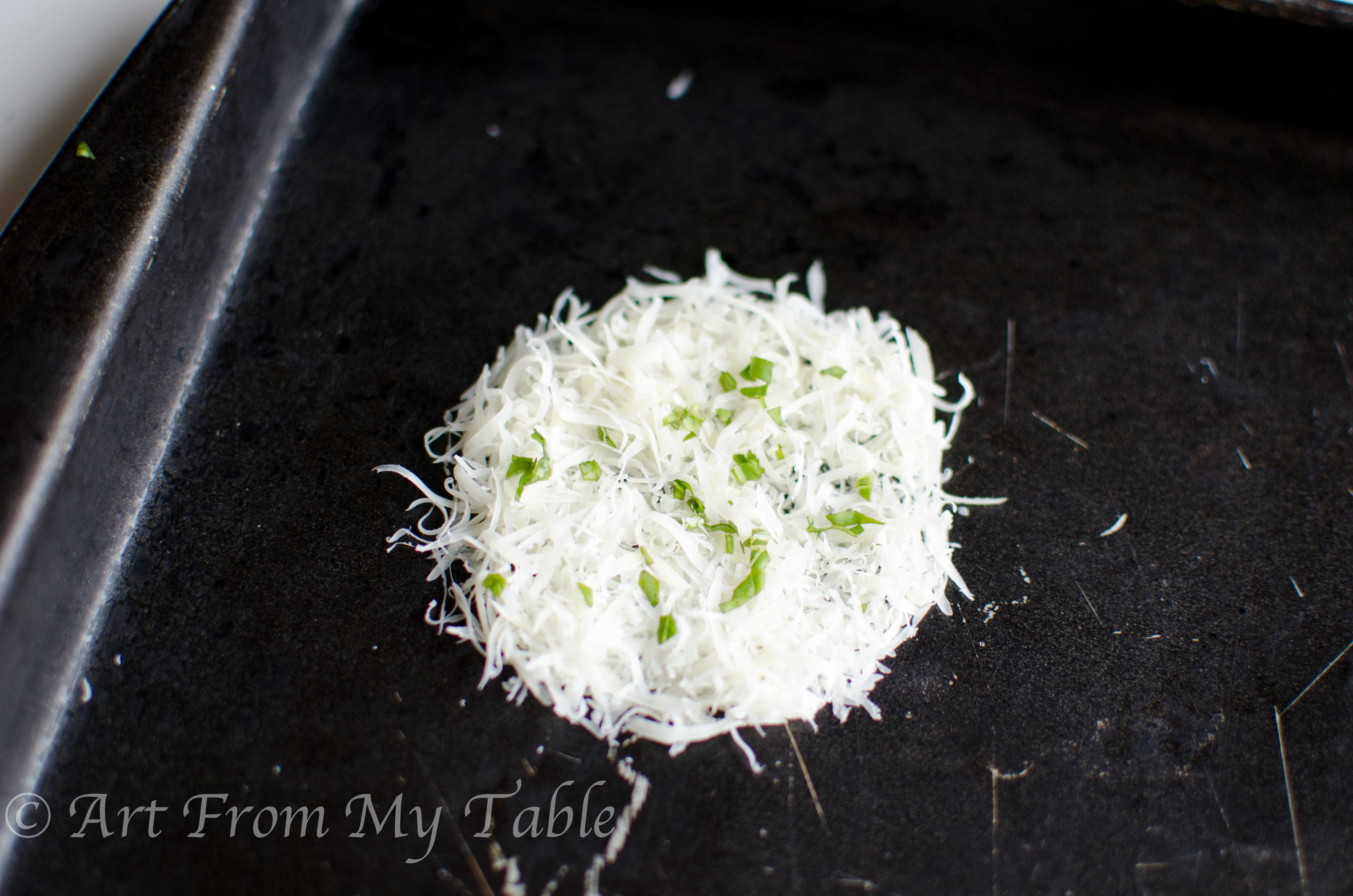 Shredded parmesan cheese formed into a circle on a baking sheet, chopped fresh basil on top.
