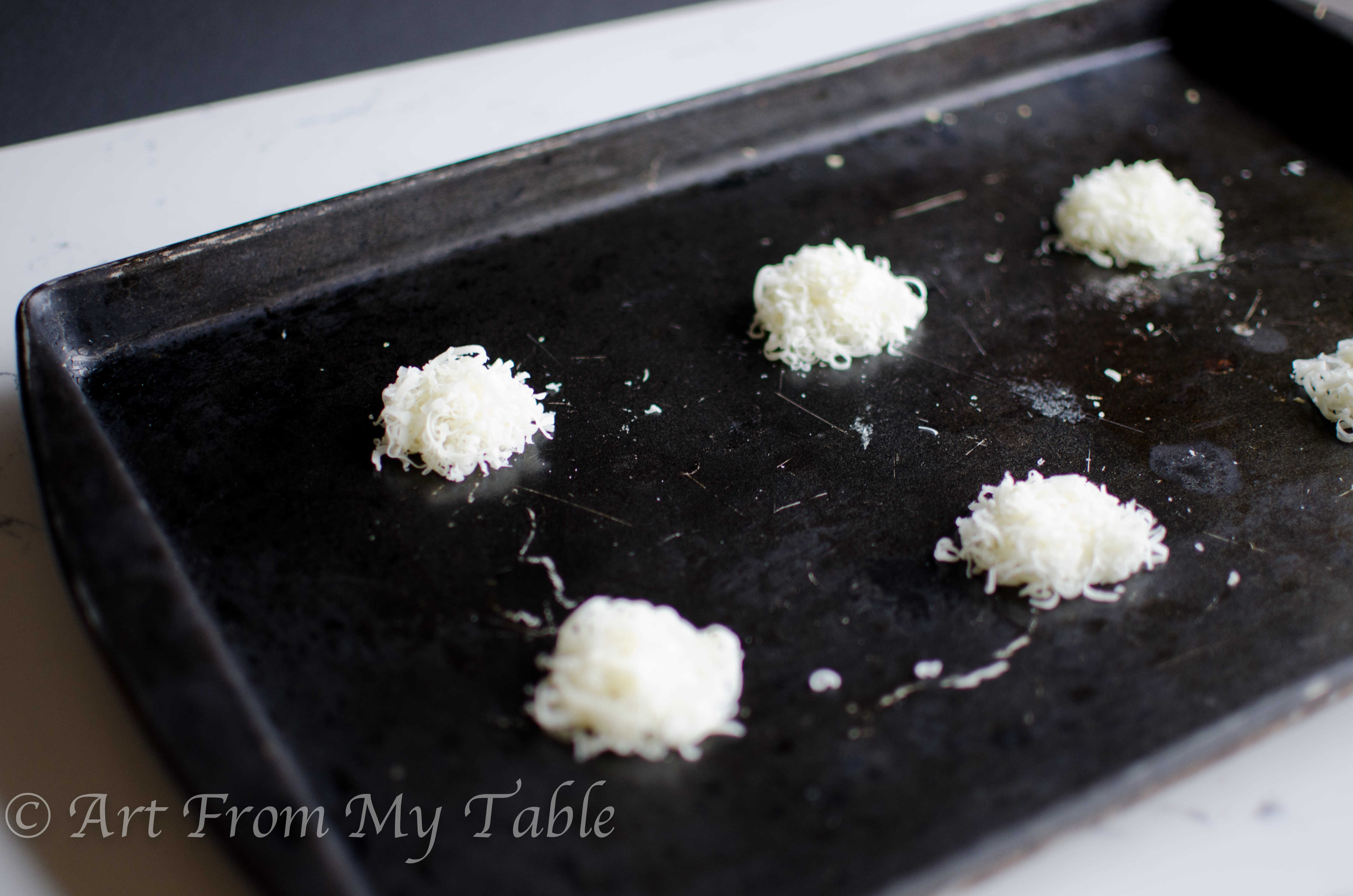 Rimmed baking sheet with shredded Parmesan cheese formed into circles.