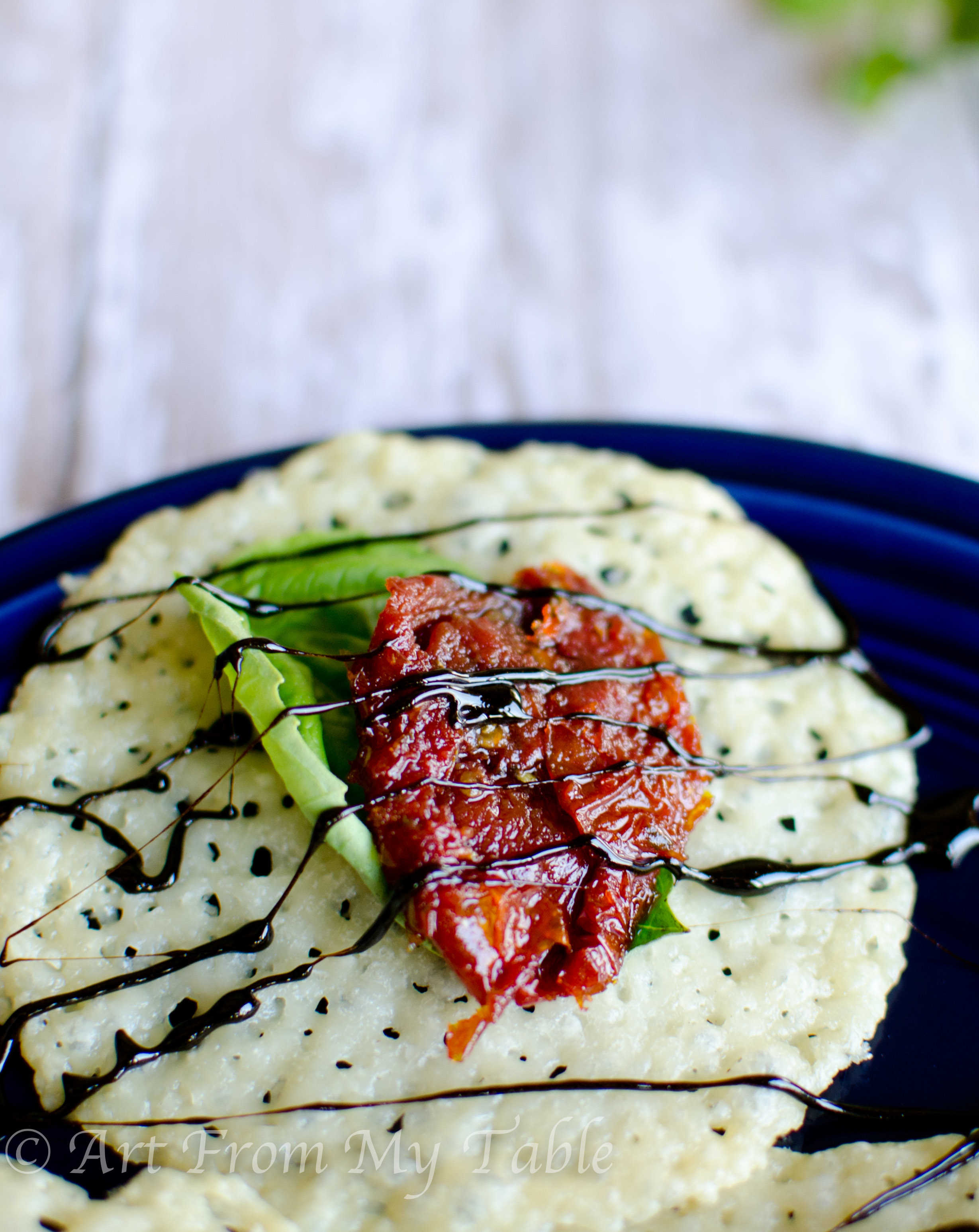 Baked Parmesan cheese crisp topped with a fresh basil leaf, sun-dried tomato, and drizzled with balsamic reduction.