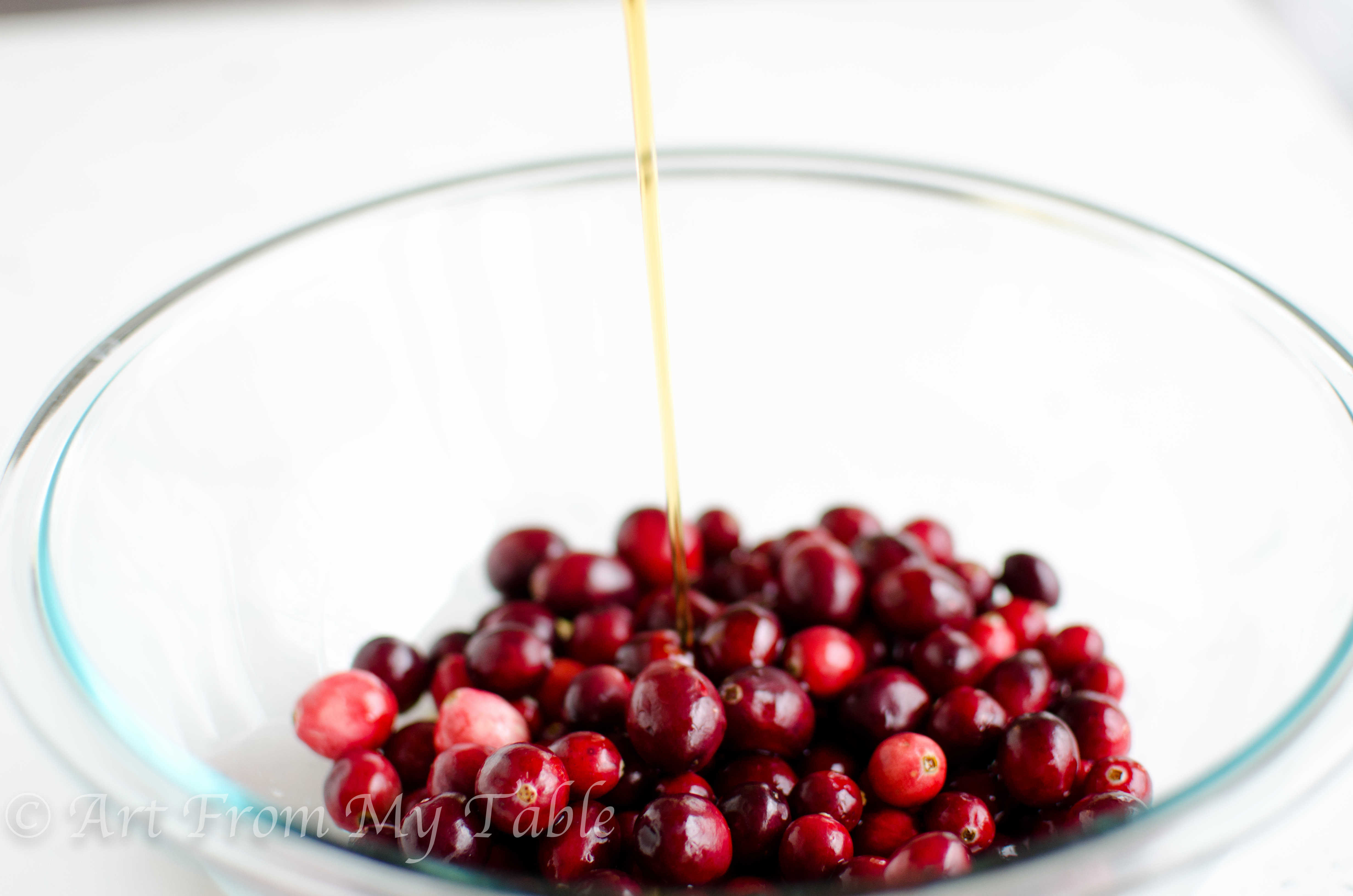 Maple syrup being poured into a bowl of fresh cranberries.