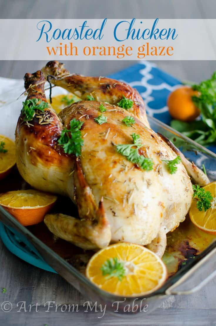 Whole roasted chicken with orange glaze garnished with parsley and orange slices.
