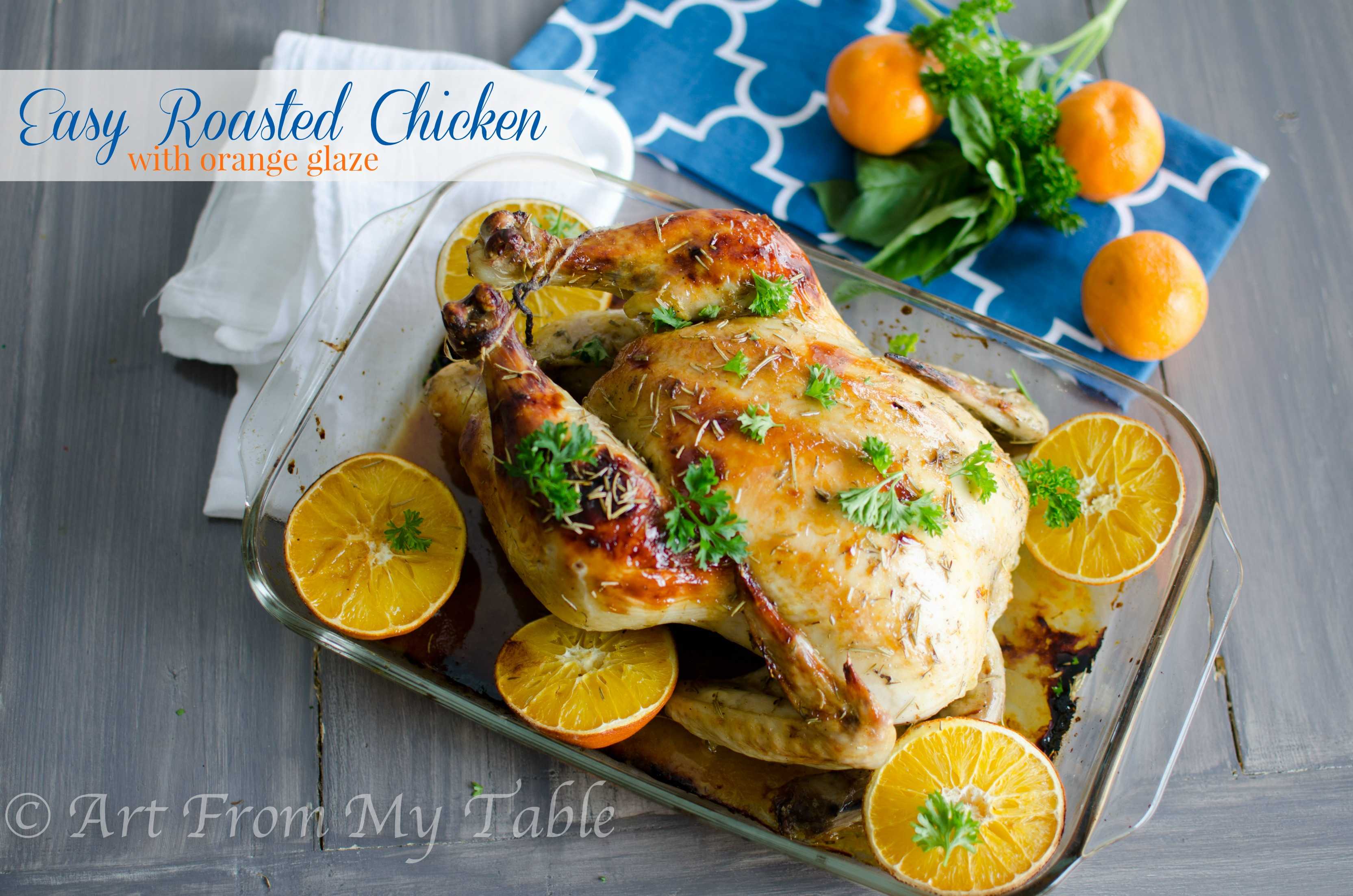 Whole roasted chicken with orange glaze in a baking dish surrounded with orange halves.