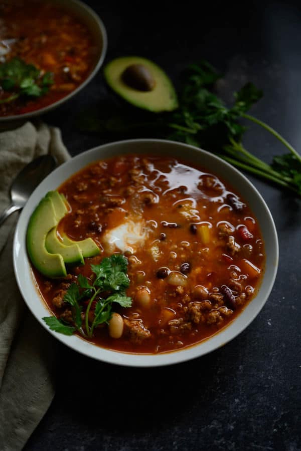 steaming bowl of turkey chili garnished with slices of avocado, cilantro and plain yogurt