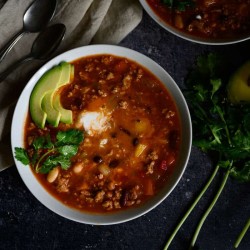 slow cooker turkey chili in a white bowl topped with cilantro, yogurt and avocado slices