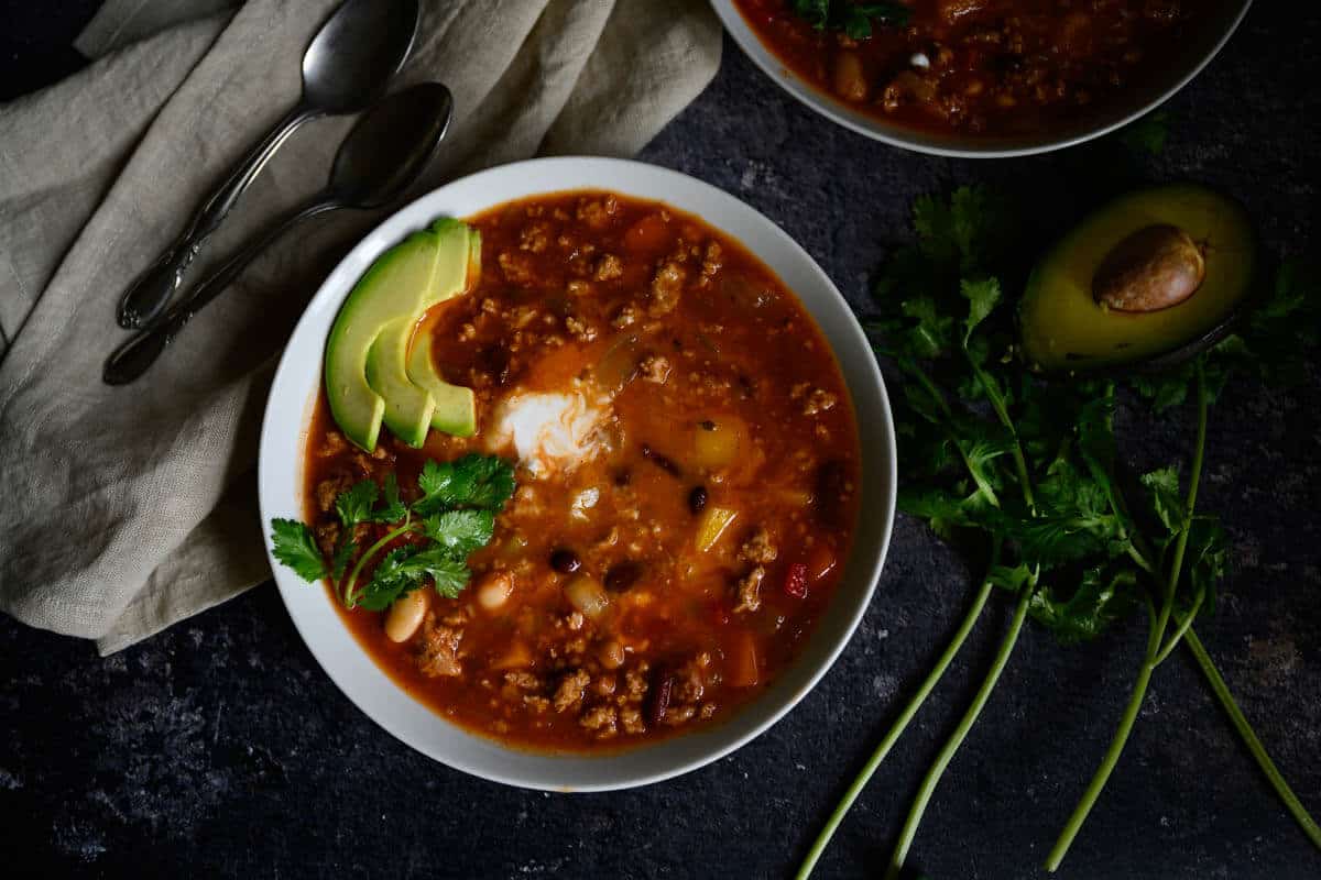 slow cooker turkey chili in a white bowl topped with cilantro, yogurt and avocado slices