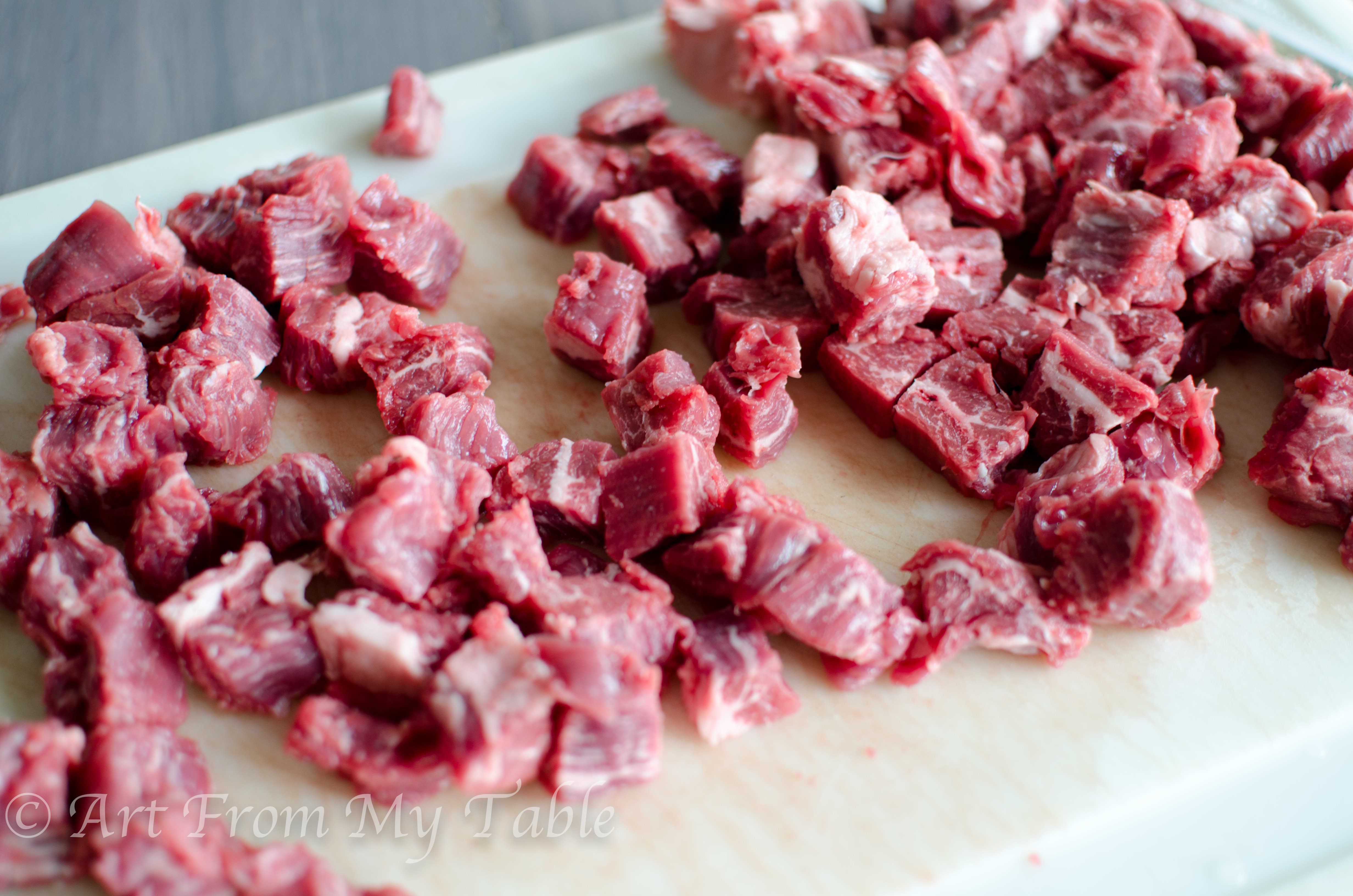 Bite sized pieces of raw steak on a cutting board.