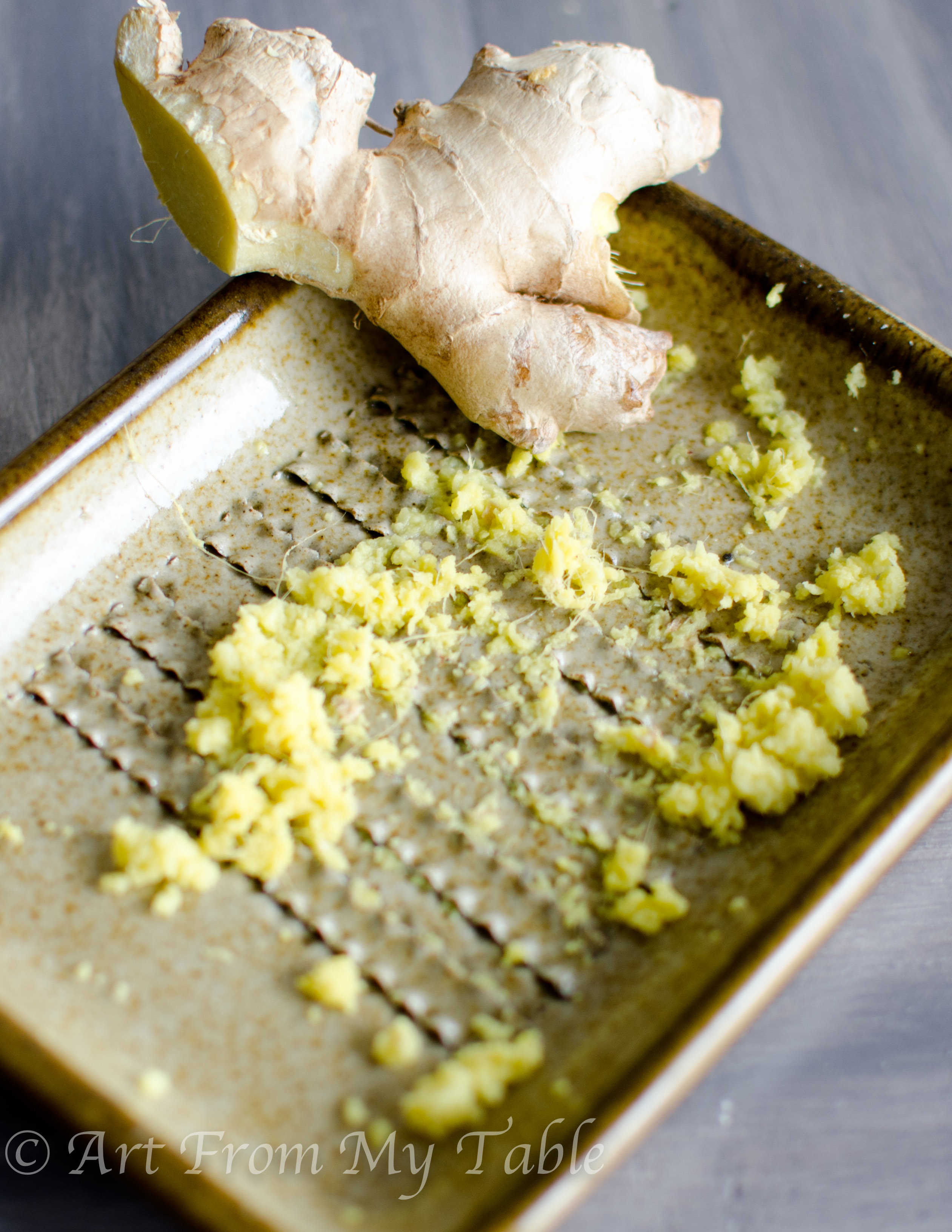 Fresh ginger root piece on a ceramic ginger grater with grated ginger.
