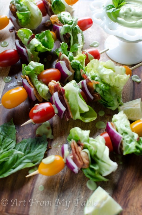 Board of Salad skewers that include lettuce, bacon, tomato, and onion, drizzled with avocado dressing.