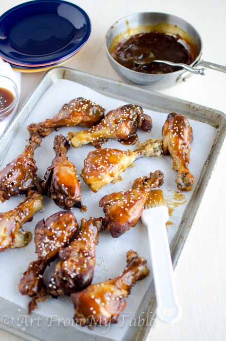 slow cooker sesame chicken drumsticks on a platter with extra sauce being brushed on.