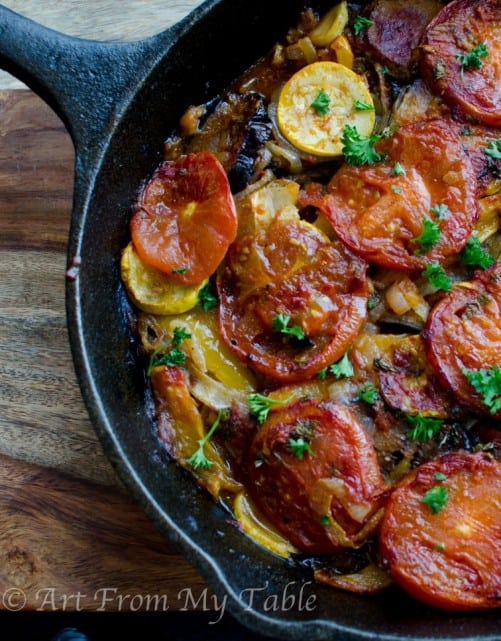 Baked eggplant, squash, potatoes, tomatoes, and more, baked in a cast iron pan topped with fresh parsley.