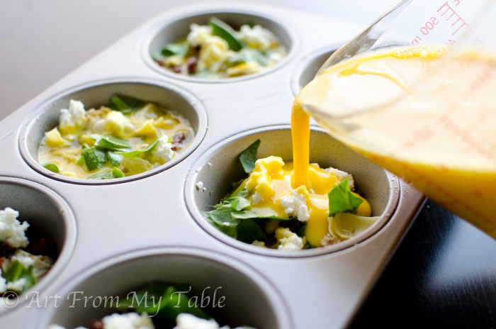 Eggs that have been blended, in a measuring cup, pouring into the wells of the muffin tin with the vegetables.