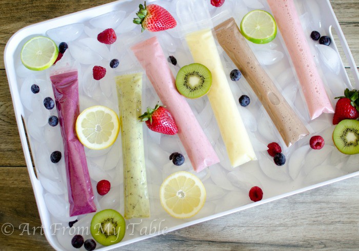 Different flavors of DIY yogurt tubes on a tray, with ice cubes and fresh fruit garnishes.