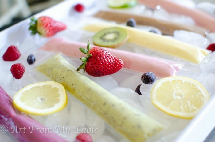 Homemade yogurt tubes in different flavors on a tray with fresh fruit.