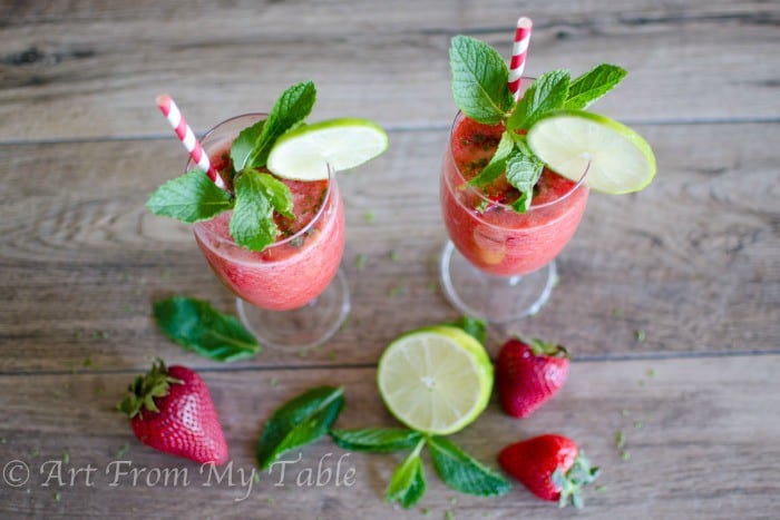 Two blended Nonalcoholic Strawberry Mojitos garnished with fresh mint and lime with red and white straws. 