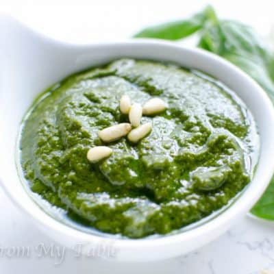 Homemade pesto in a white ceramic dish garnished with a few pine nuts.
