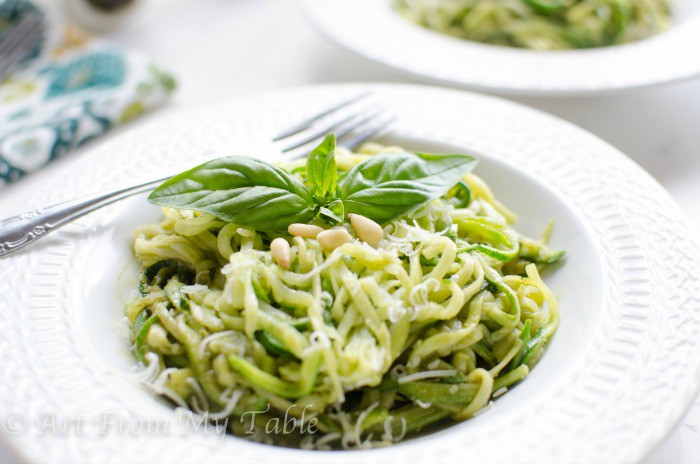 Bowl of Zucchini noodles with pesto sauce, pine nuts, and fresh basil.