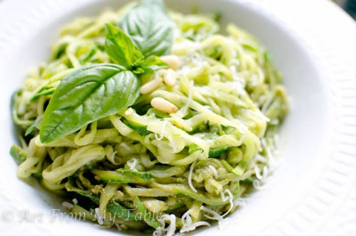White bowl of Zucchini noodles with homemade pesto and parmesan cheese. 