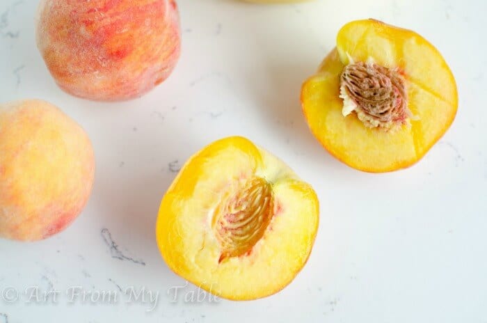 1 peach sliced in half with a few whole peaches nearby.