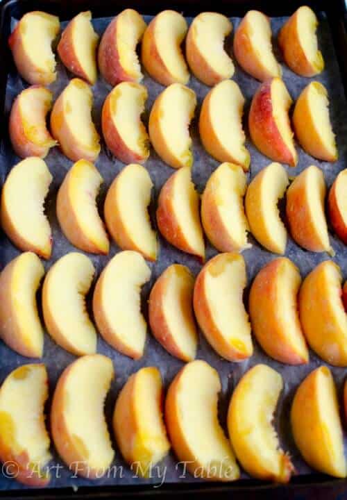 Slices of fresh peaches neatly lined on a rimmed baking sheet lined with parchment paper ready to be put in the freezer.