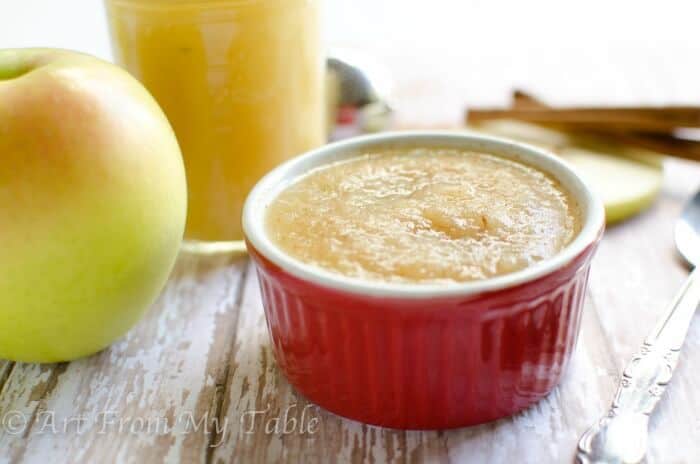 Sugar-free Homemade Applesauce in a red ramekin with apples and cinnamon in the background.