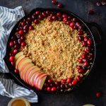 healthy apple crisp baked in a cast iron skillet topped with fresh cranberries and fresh apples